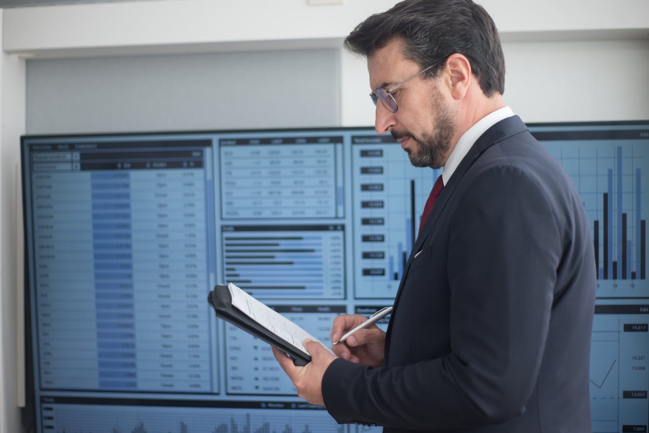 about-07 Businessman in a suit analyzing data analytics on large screens, taking notes.